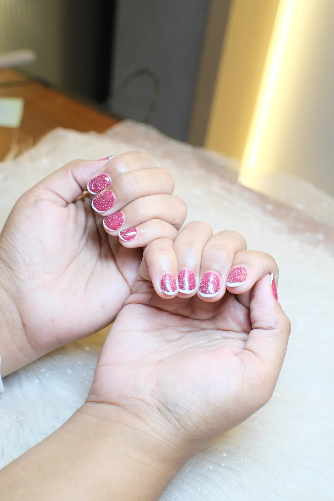 Hasil nail pink glitter dengan garis tepi putih pada kedua tangan.