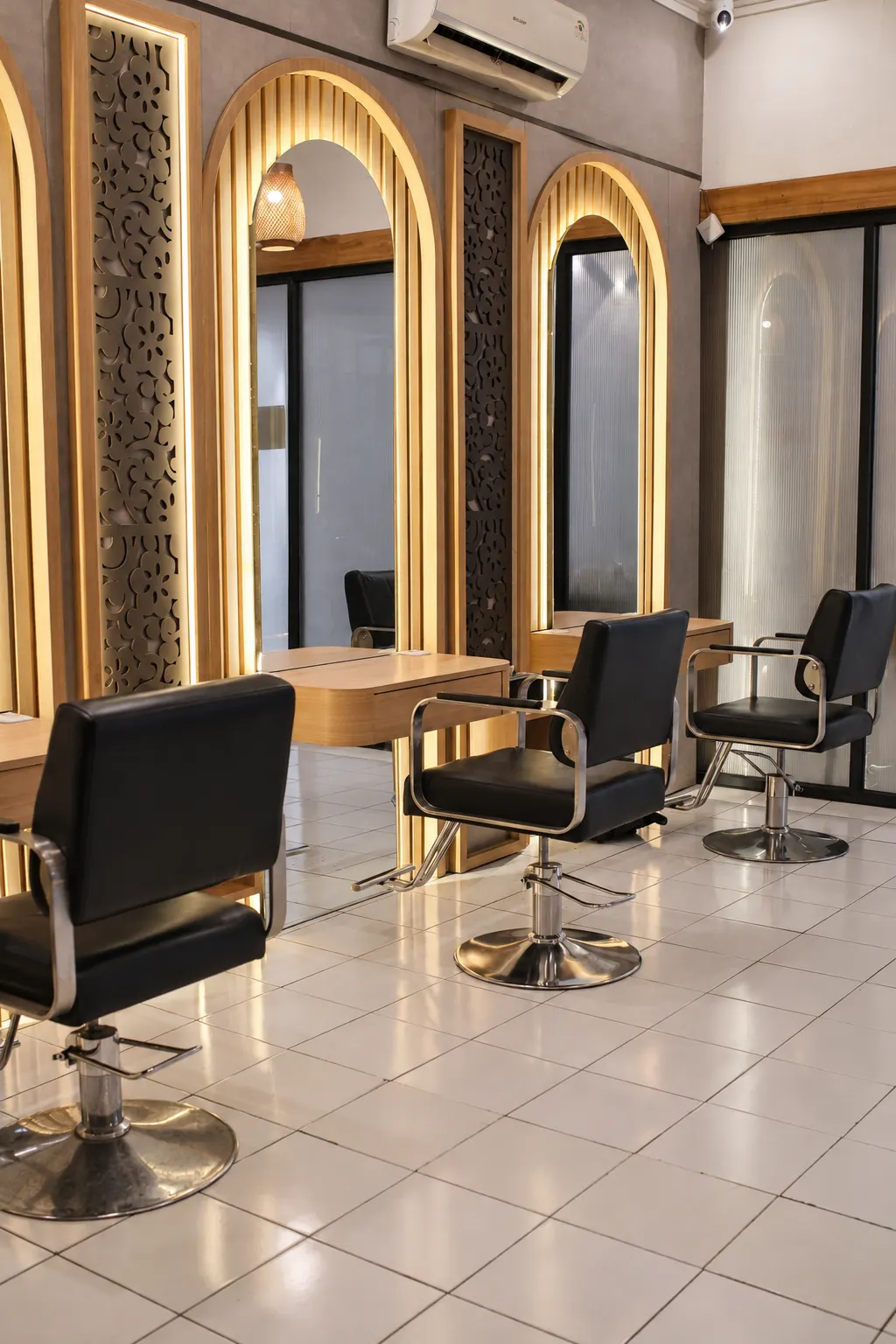 Deretan kursi styling dan cermin berbingkai kayu dengan pencahayaan hangat di Gussy Salon.