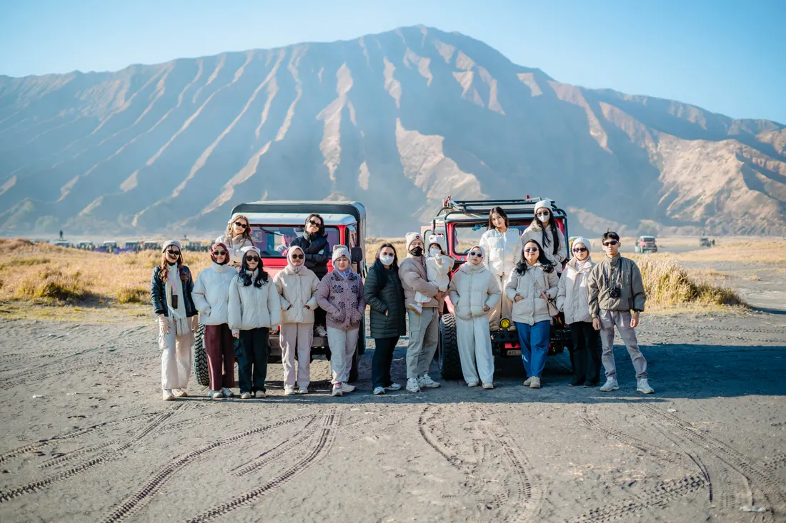 Tim Gussy berfoto bersama saat liburan dengan latar pegunungan dan kendaraan wisata.